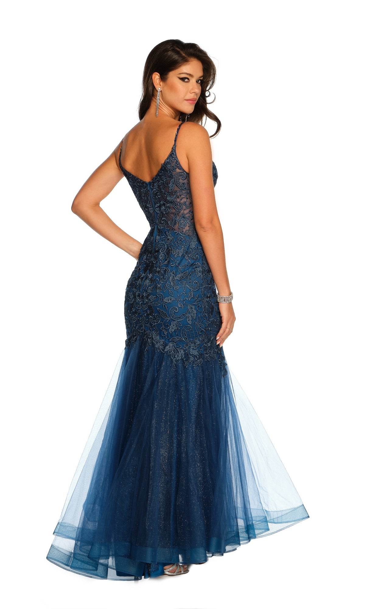 A woman in the Dave & Johnny A10625 Long Lace Mermaid Prom Dress, fitted and floor-length in navy blue with spaghetti straps, embroidered lace, and tulle accents, stands gracefully looking over her shoulder.